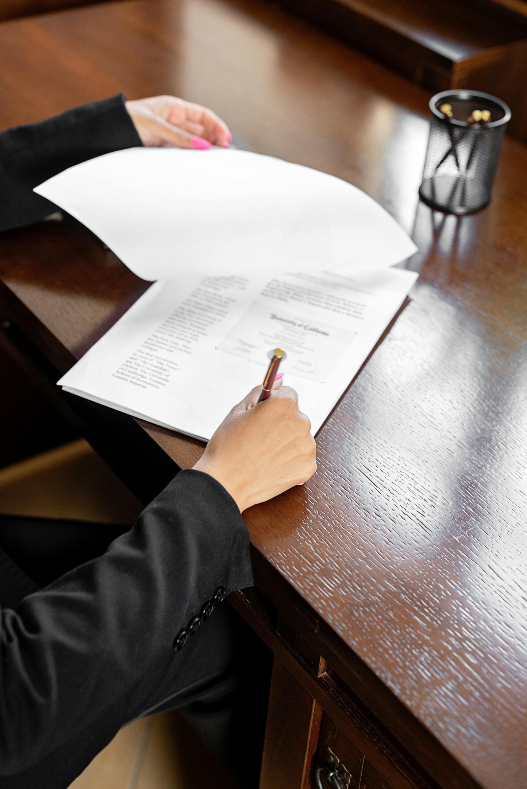 Person in a suit signing a formal multi-page contract on a dark wood desk