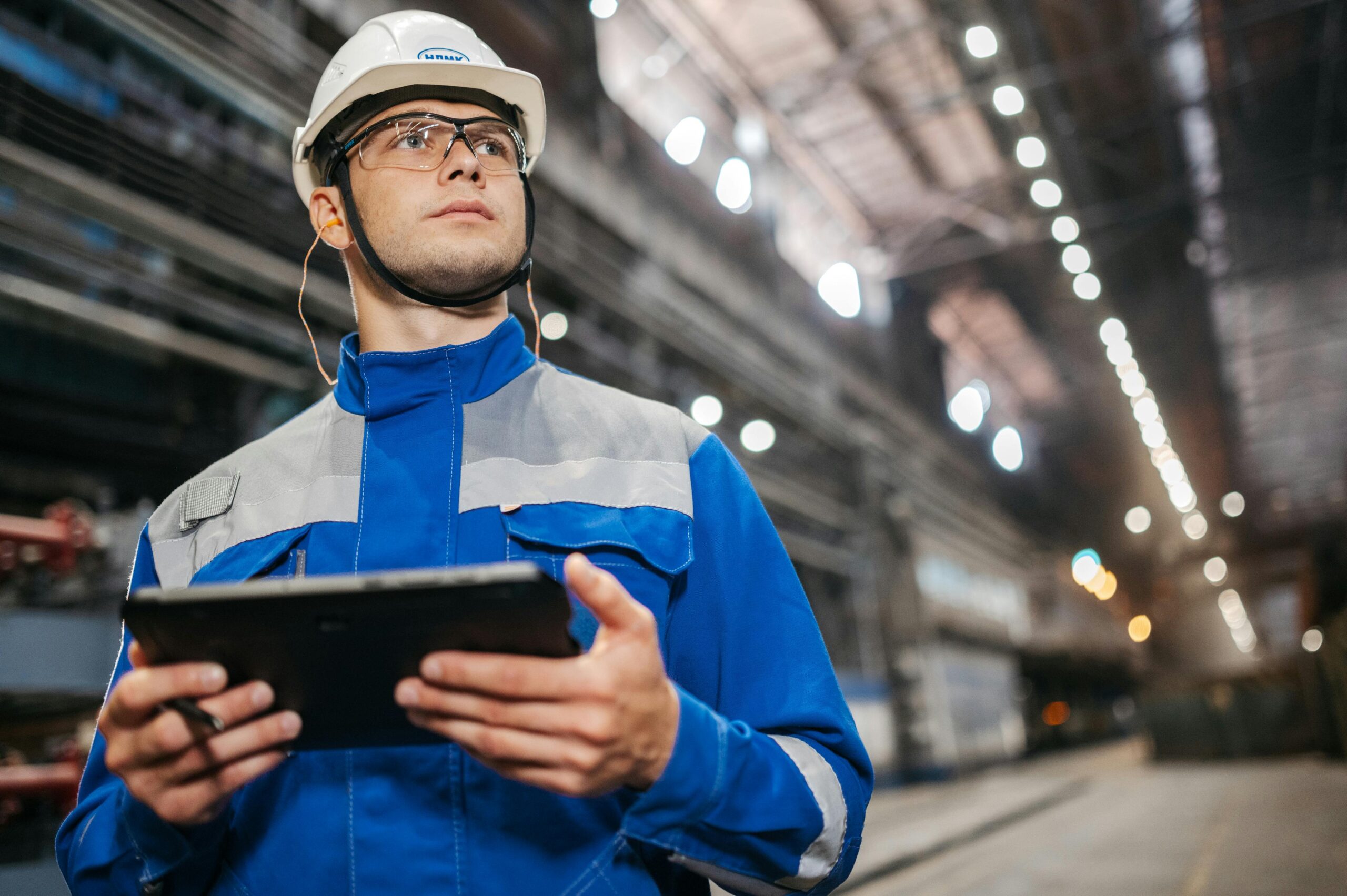 Industrial worker in blue coveralls and white hard hat reviewing data on a tablet
