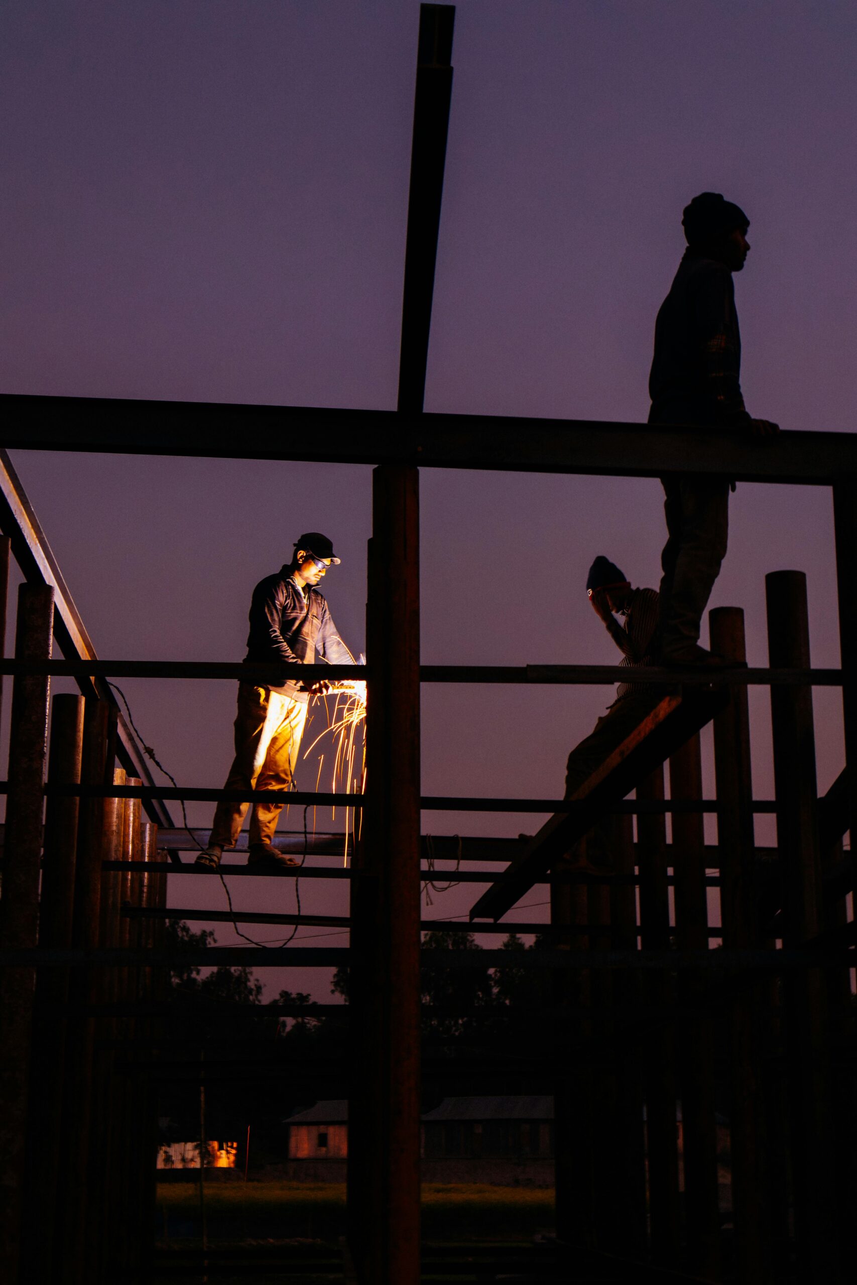 Workers on steel scaffolding at night with welding sparks